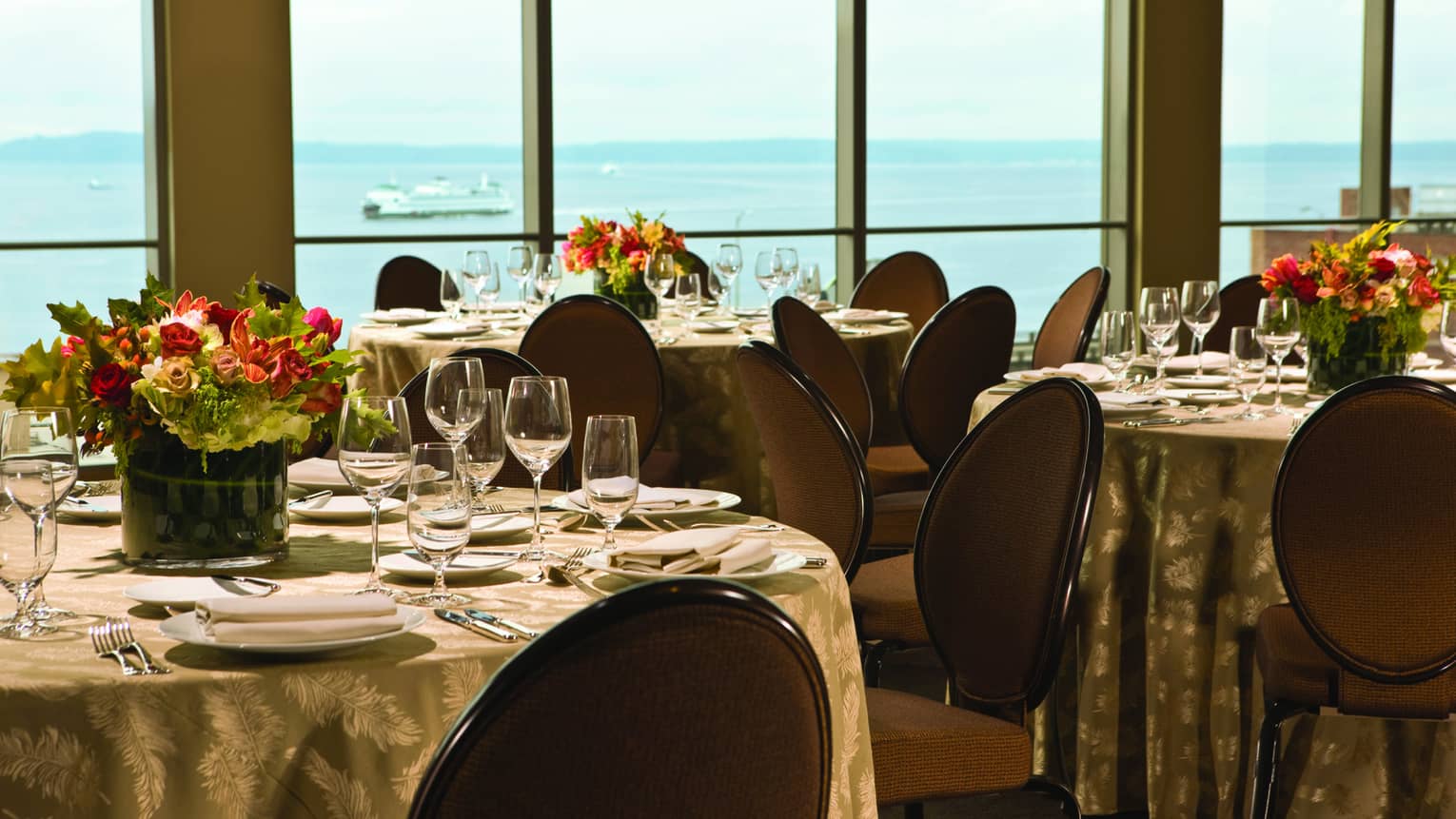 Round banquet dining tables with flowers by sunny windows with ocean views 