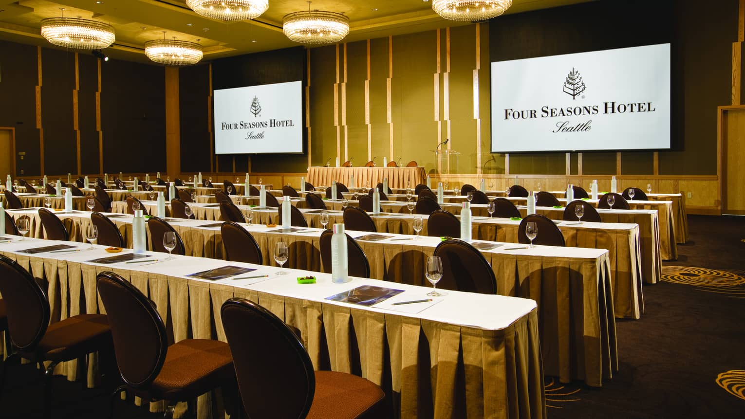 Conference in ballroom with rows of meeting tables and chairs facing two screens