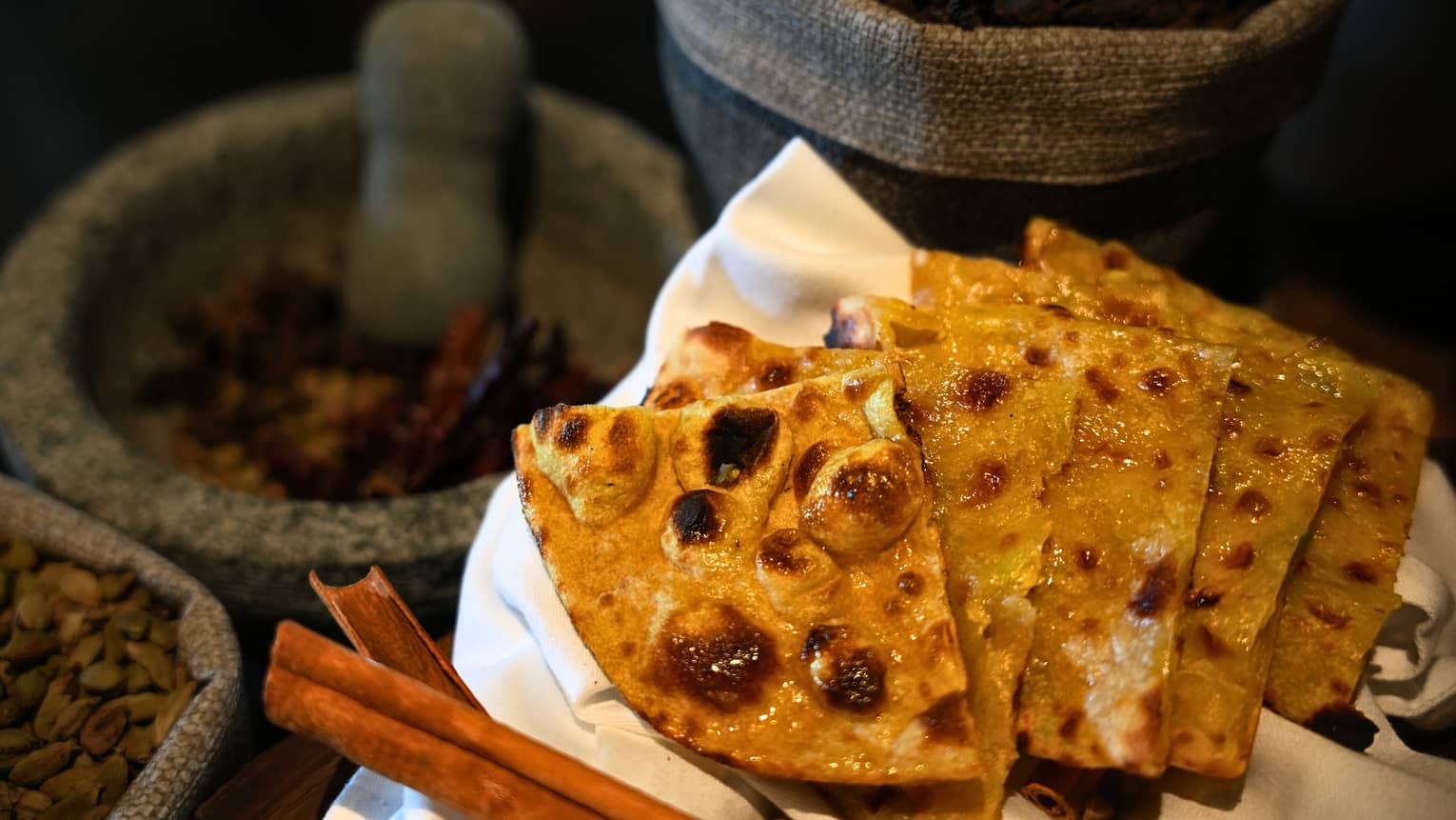 Quartered pieces of flatbread on a white cloth, with containers of spices in the background