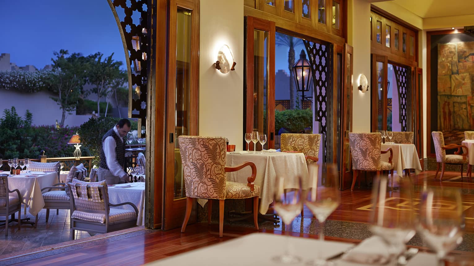 Il Frantolo Italian Restaurant, server sets patio table at night near open wall to dining room