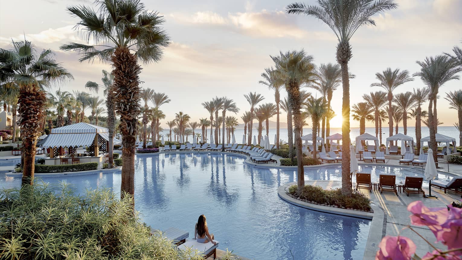 Person sits on side of luxury hotel pool surrounded by palm trees