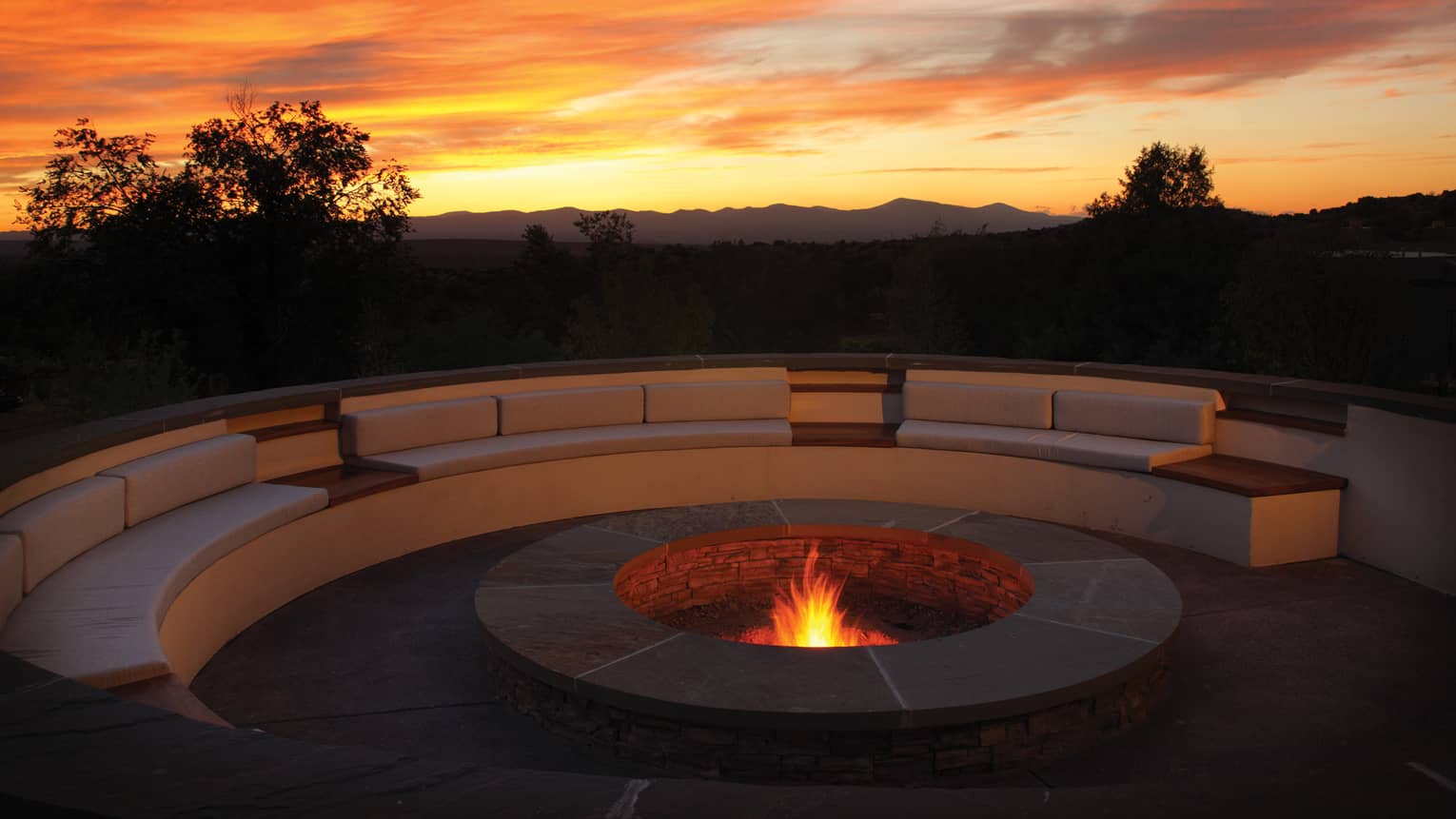 Outdoor fire pit burning with a large curved sofa, colourful sunset in the sky