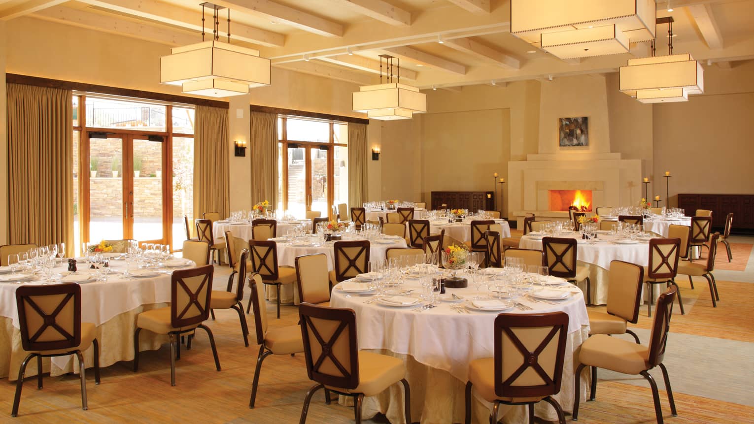 Ballroom with round tables and chairs, contemporary lighting and decor, stone fireplace, floor-to-ceiling windows 