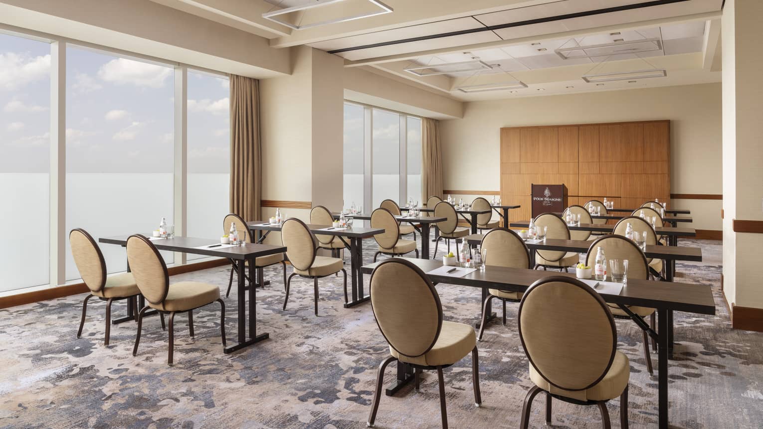 A room with small tables and chairs and large windows.