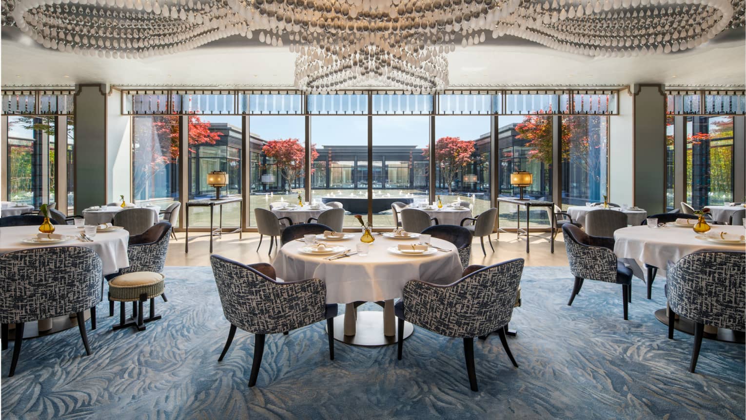 Jin Jing Ge restaurant at Four Seasons Hotel Suzhou. Dining tables with white tableclothes sit beneath a ceiling of modern chandeliers.