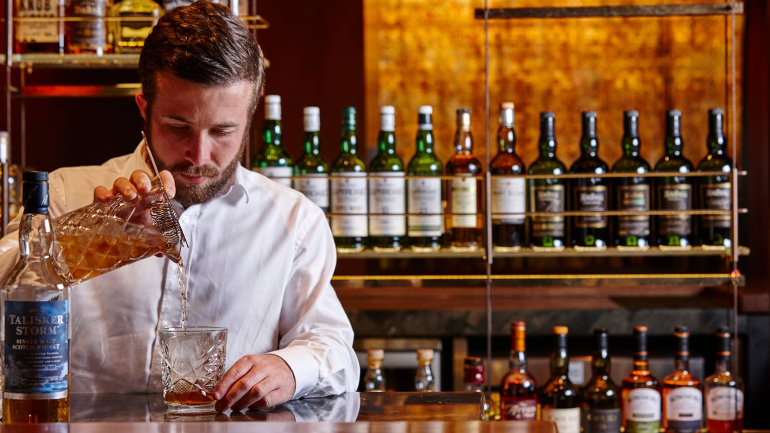 Grain bartender pours single malt whisky from crystal pitcher into glass