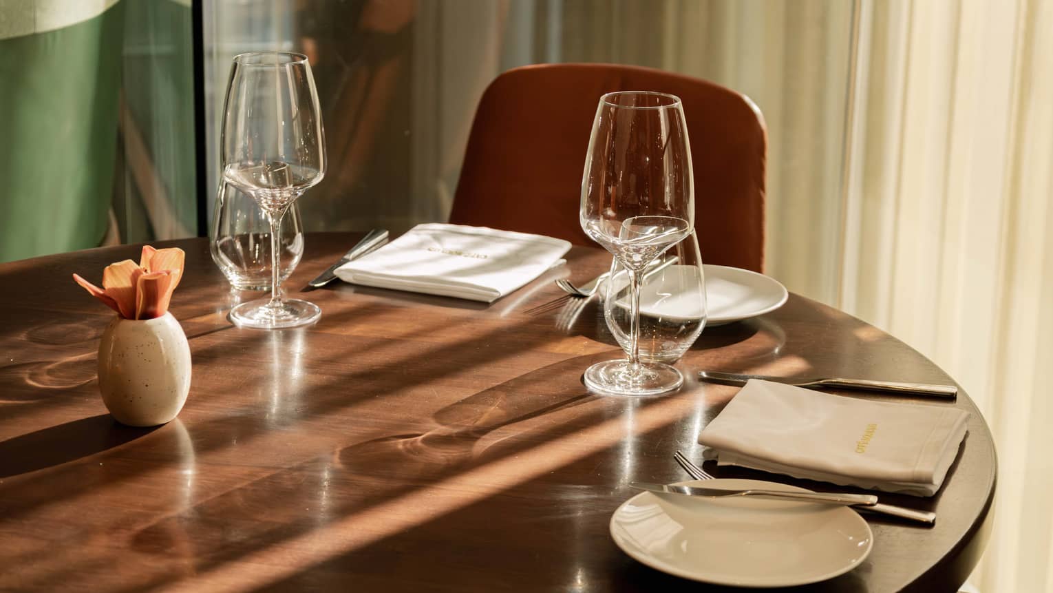 A wood dining table set with plates, napkins, utensils and glassware