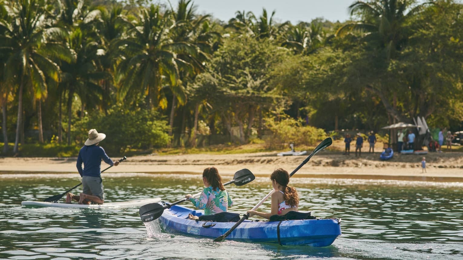 A group kayaking while a group watches from a beach.