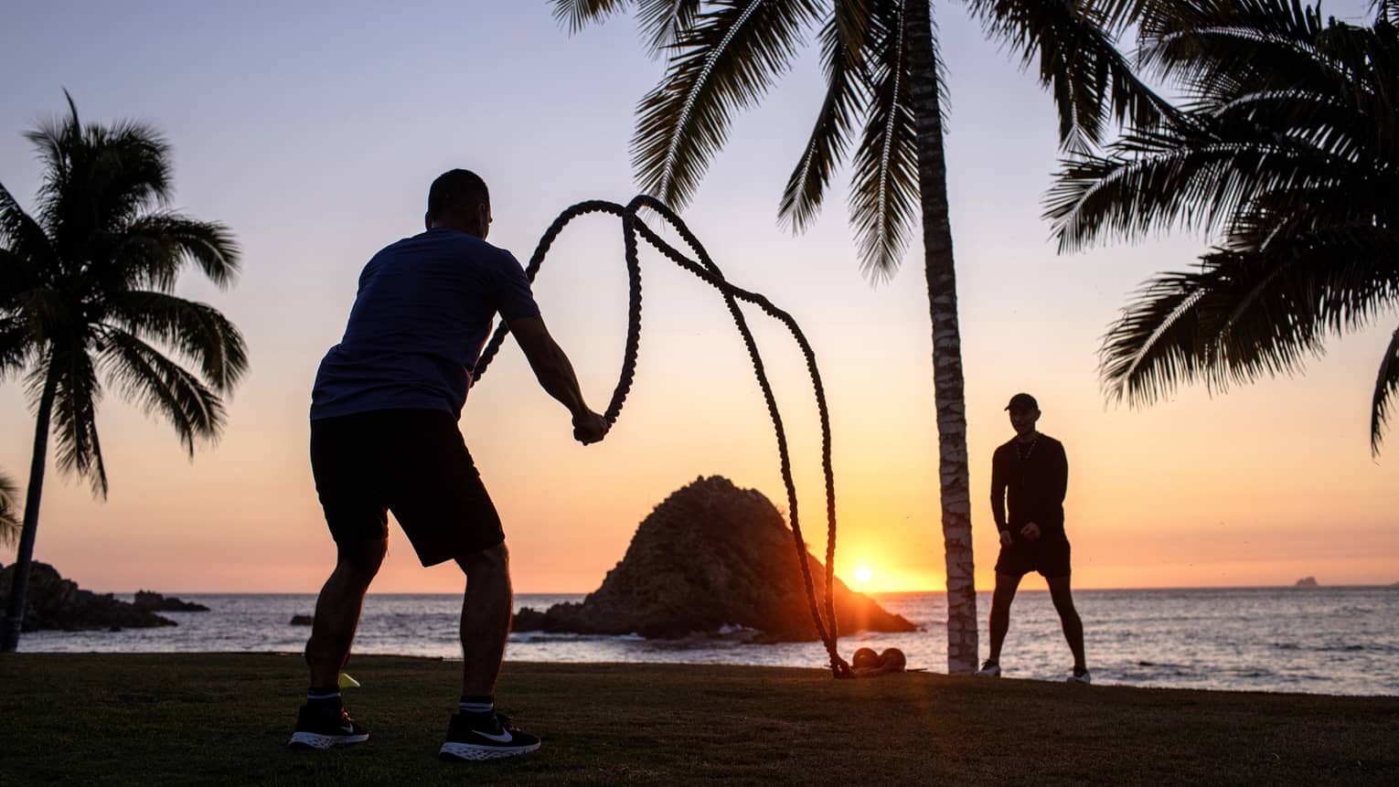 Two guests exercising using gym ropes near the ocean at sunset.