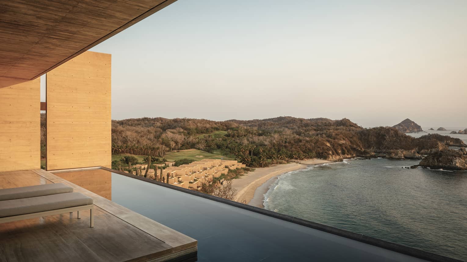 A serene beachfront view from a minimalist luxury villa with an infinity pool, overlooking a secluded beach, rolling hills and the ocean at sunset