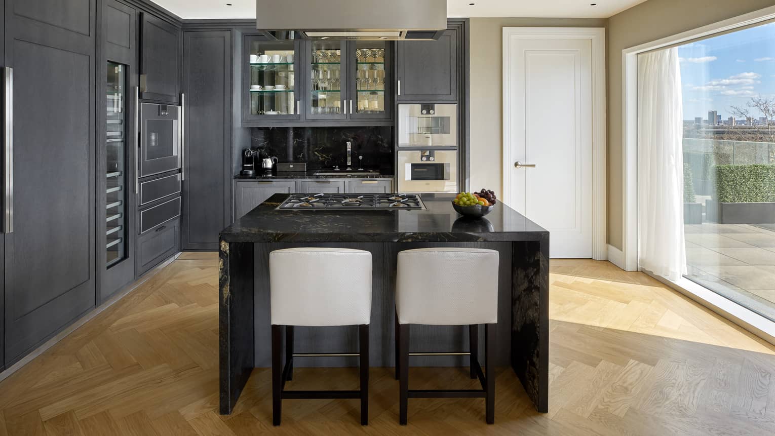A kitchen area with dark walls, large dark island, stools and large window.