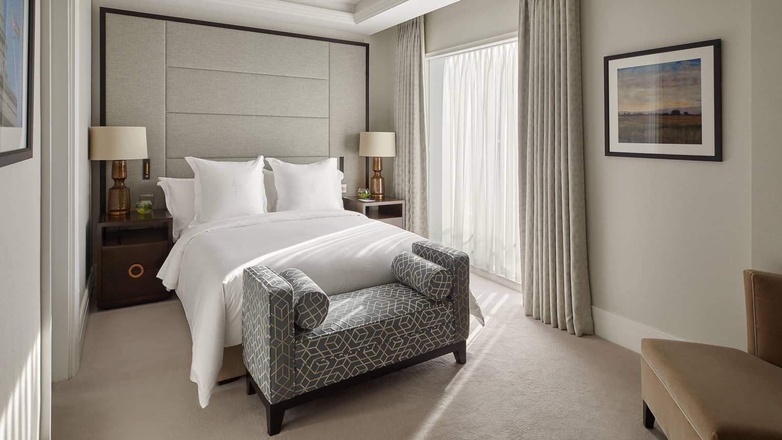 A room with a bed, bench, chair and two side tables.