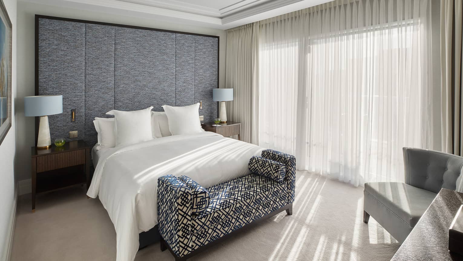 A bed, two side tables with lamps, a bench and a chair.