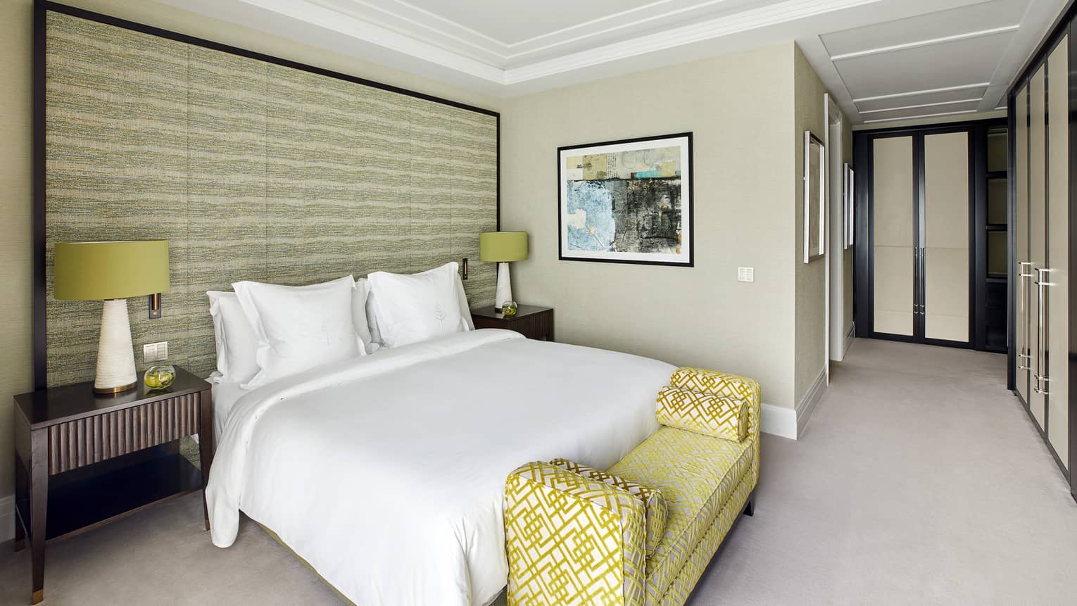 A room with bed, bench and two side tables with lamps.