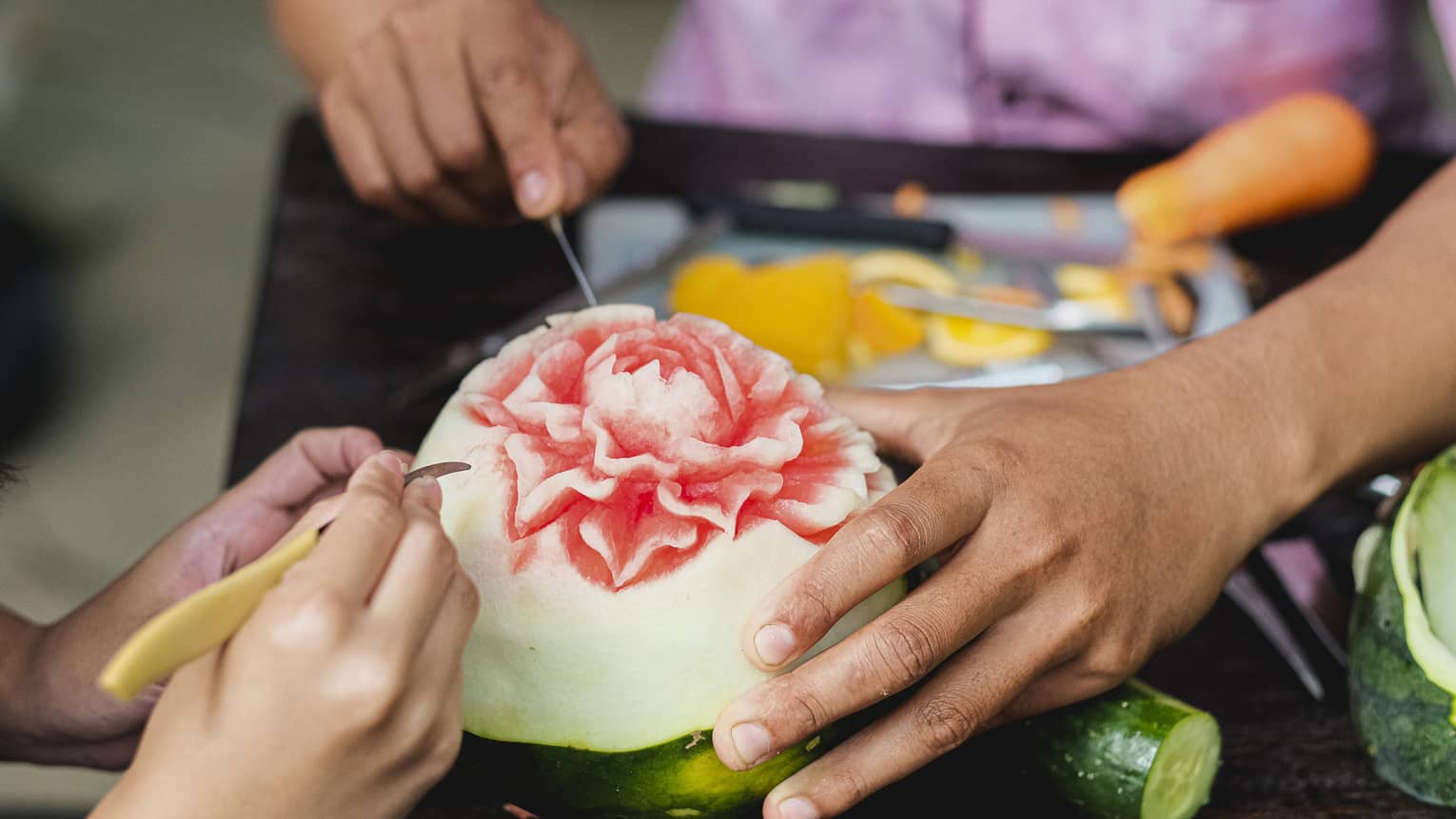 Close-up shot of man and child's hands carving intricate flower into watermelon