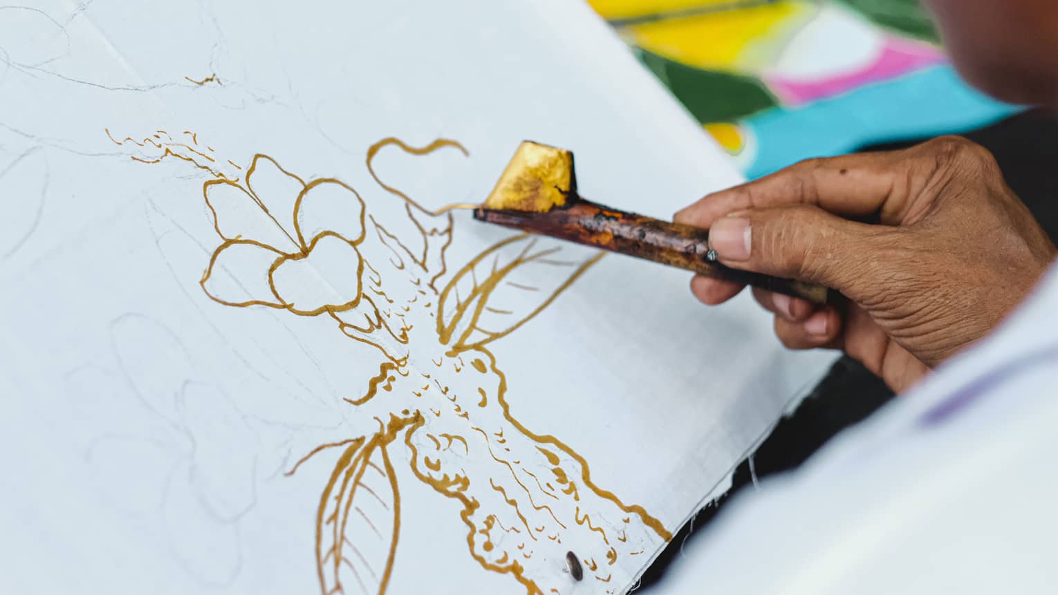 Close-up of man's hand doing batik painting on white canvas