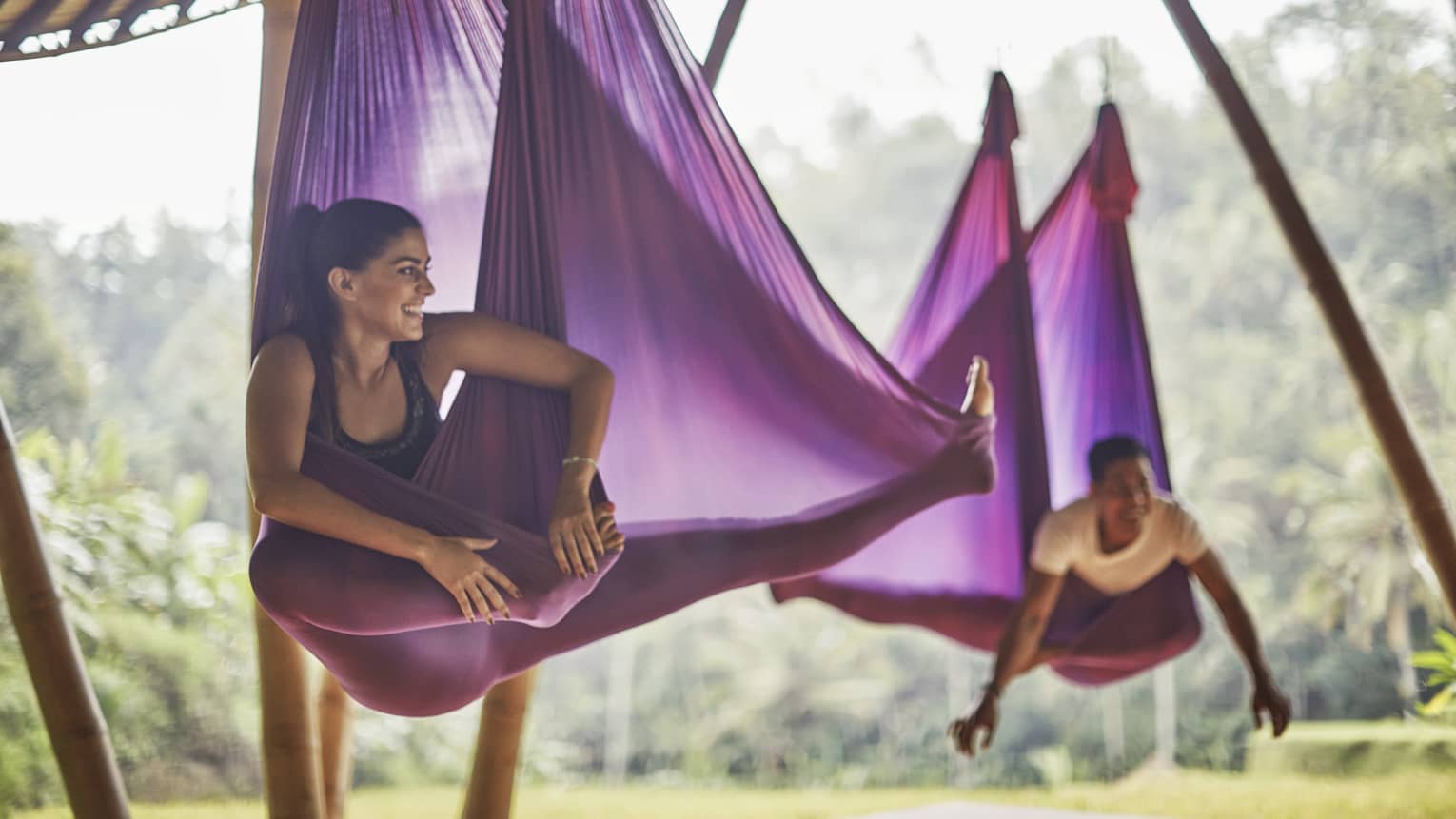 Guests hold yoga stretches while suspended in aerial silk hammocks, the forest sprawling behind them. 