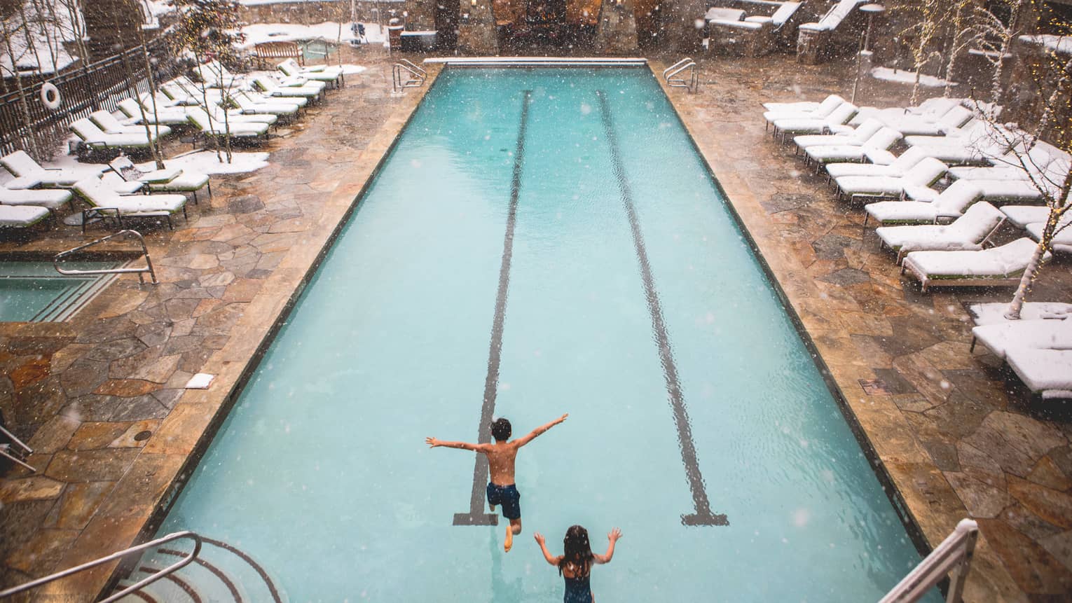 Two children jump into the heated pool on a snowy day at Four Seasons Vail 