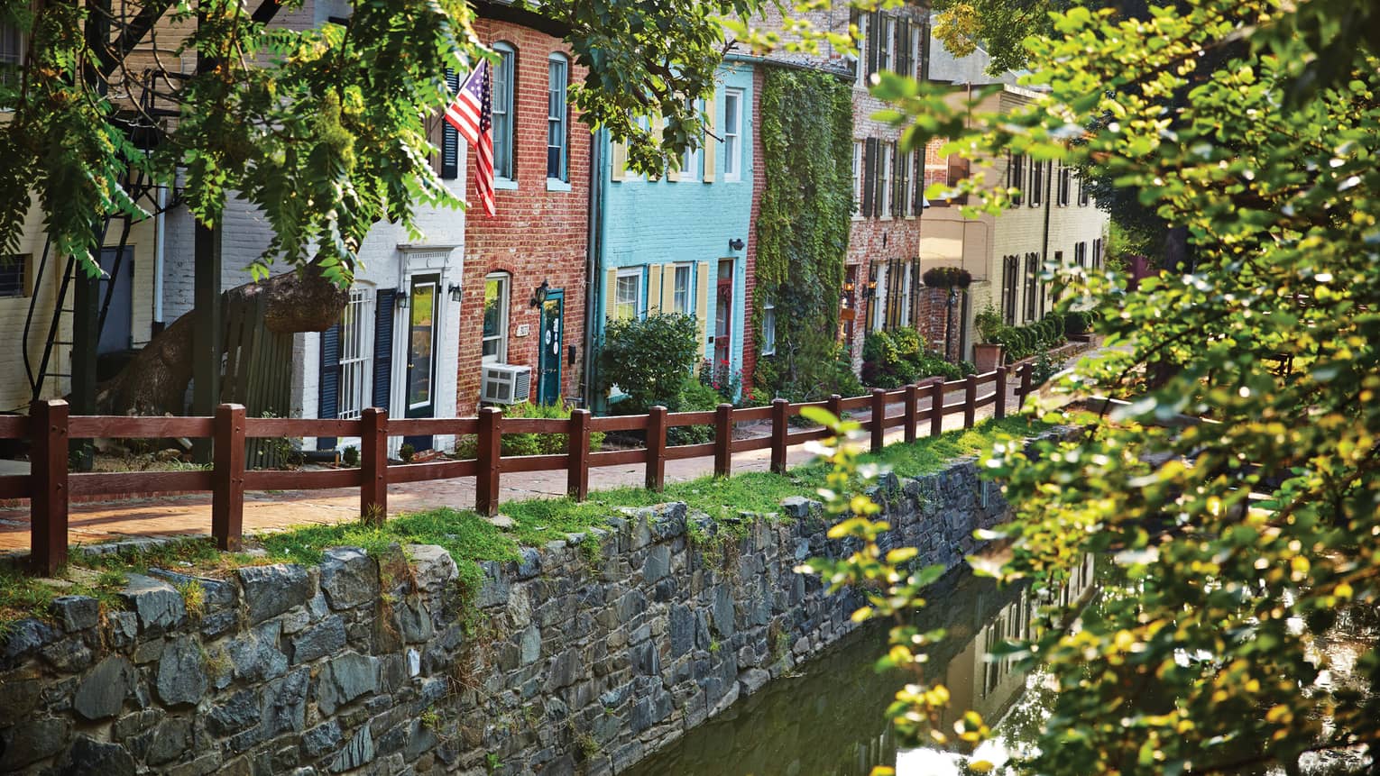 Row of colorful houses in city, road and wooden fence along a canal with trees