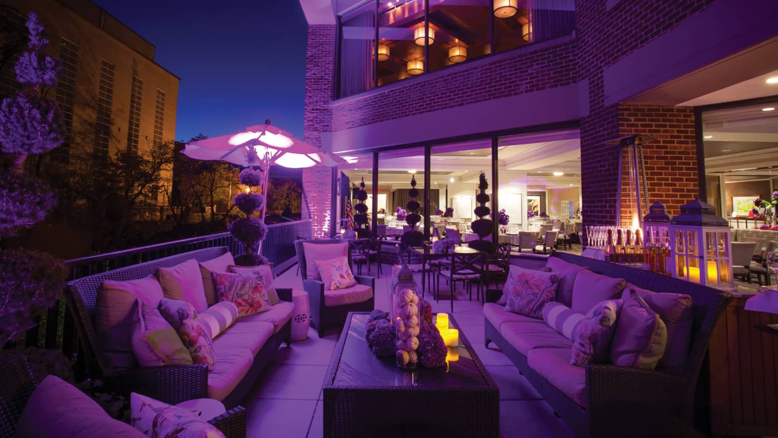Outdoor Seasons at night with patio banquette lounge chairs, table and sofa, purple hue 
