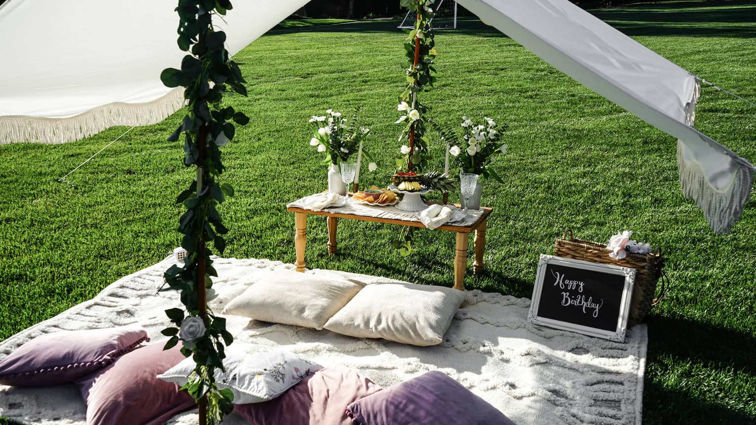 Picnic set up with a blanket, pillows, table, flowers and white canopy