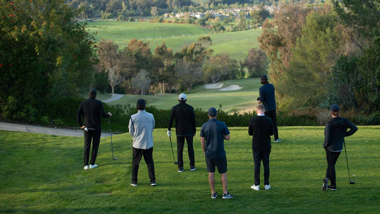 Seven people stand on a putting green overlooking a golf course with green rolling hills in the distance