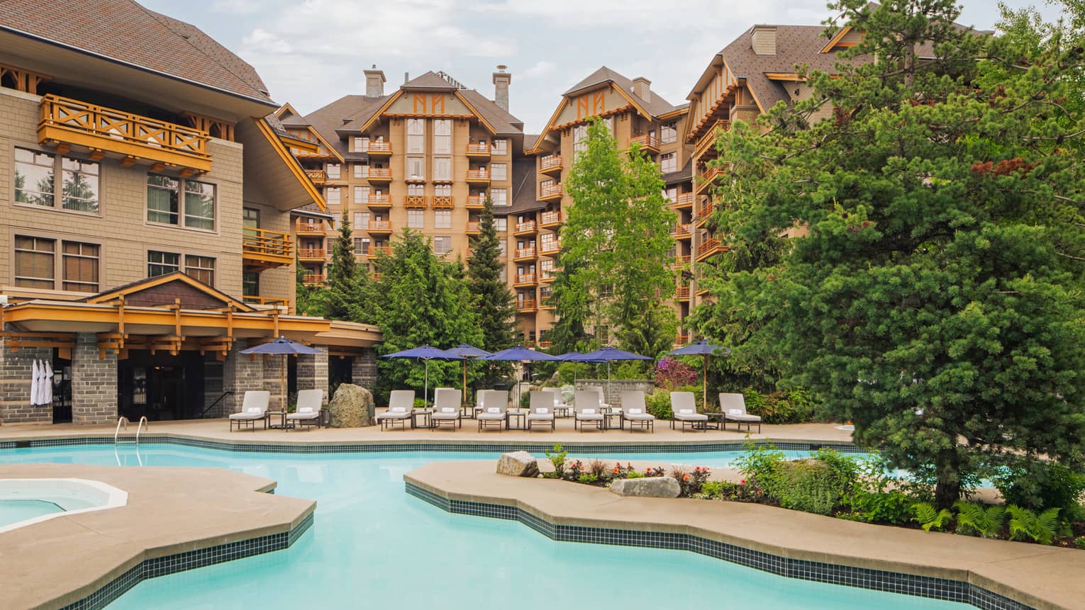 An outdoor pool next to a large hotel building with trees near the pool.