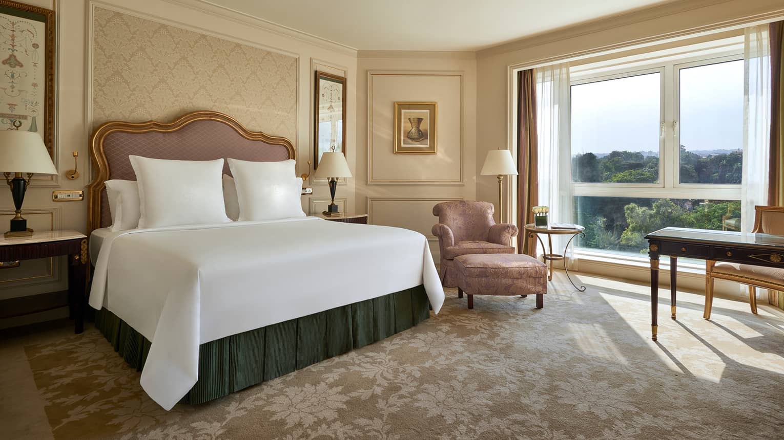 Deluxe Room bed with upholstered pink headboard, gold pattern wallpaper, pink silk armchair by sunny window