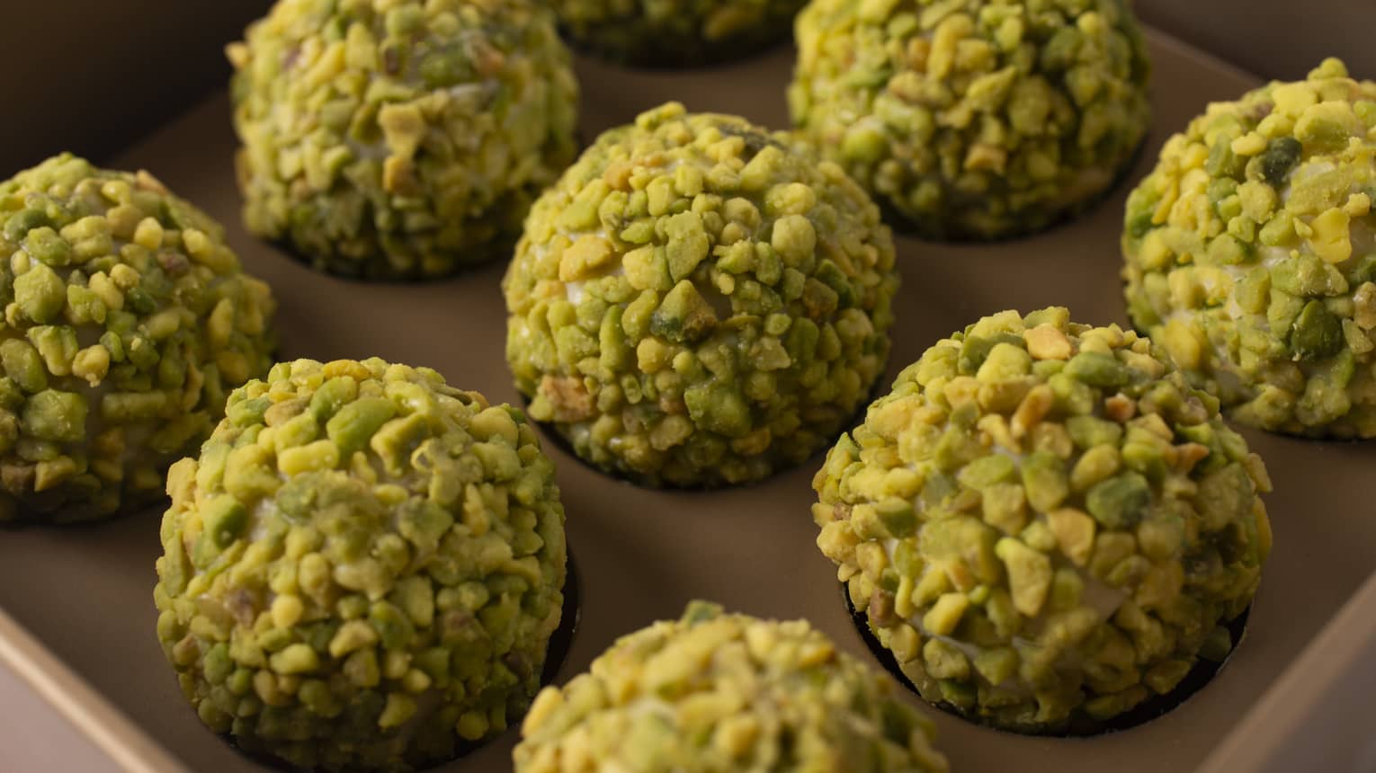 Nine pistachio-coated chocolate truffles lined up in rows of three