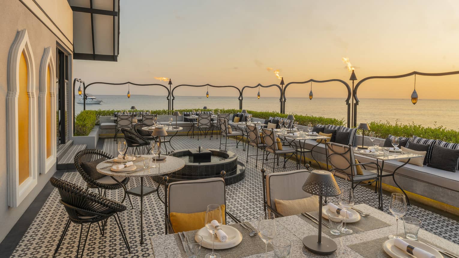 Outdoor terrace of Al Barakat at sunset with round and square tables, rattan chairs, string lighting
