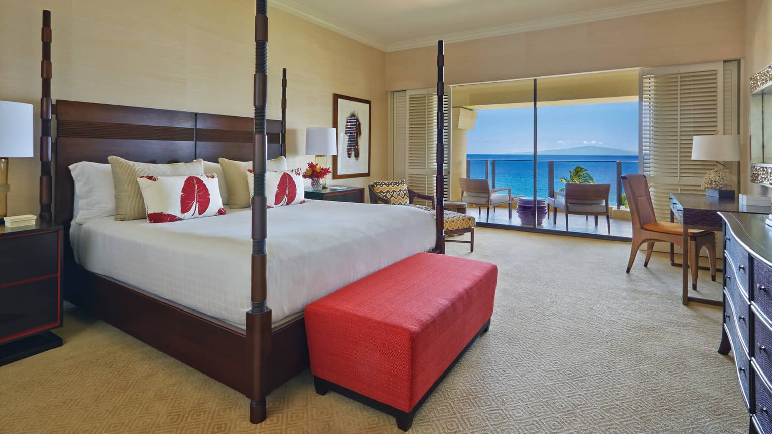 Luxury bedroom with a four-poster bed, red bench and balcony offering ocean view at a tropical resort suite