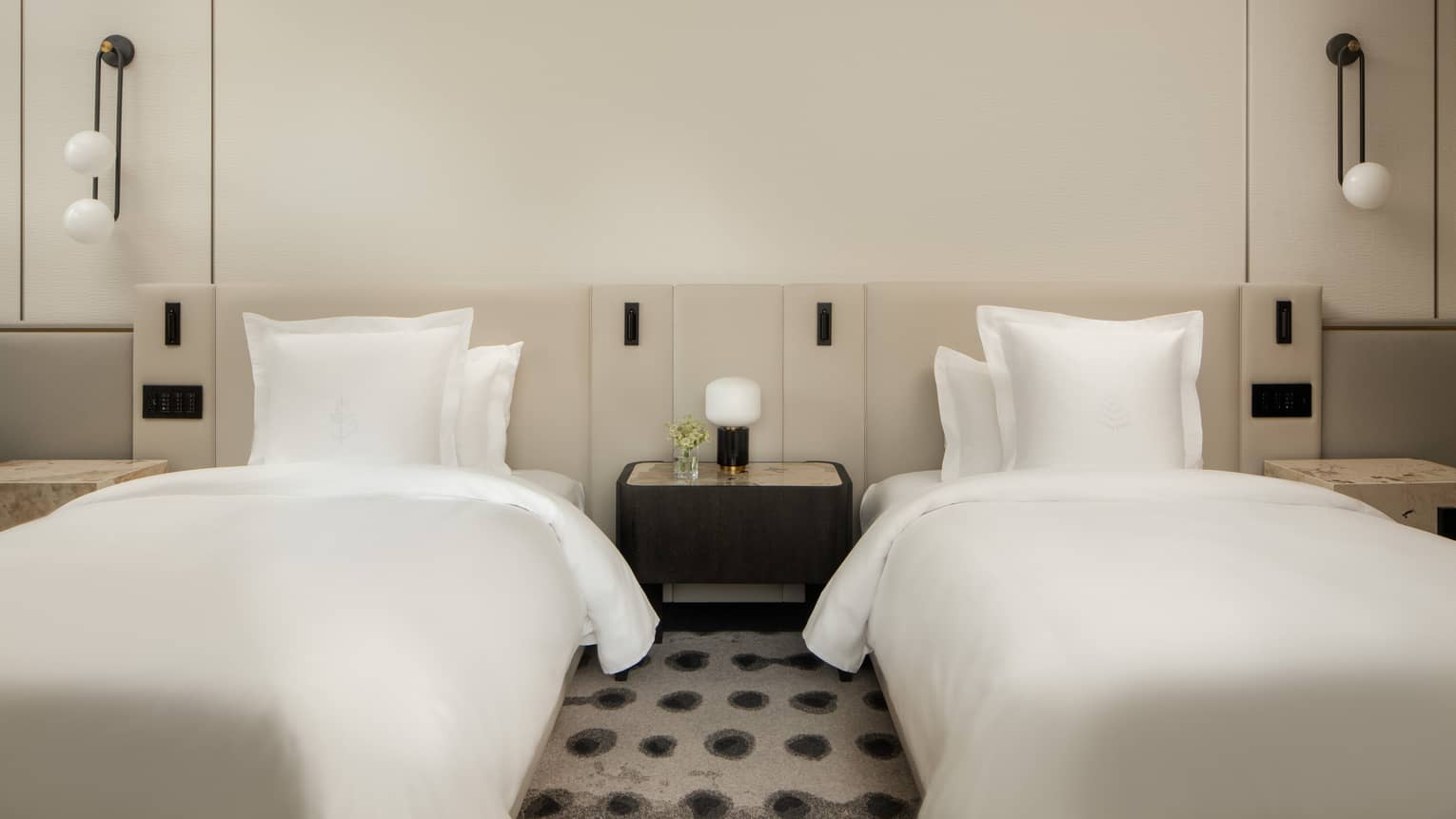 Luxury hotel room with two double beds, white linens, a shared nightstand, wall-mounted lights, featuring minimalist décor 