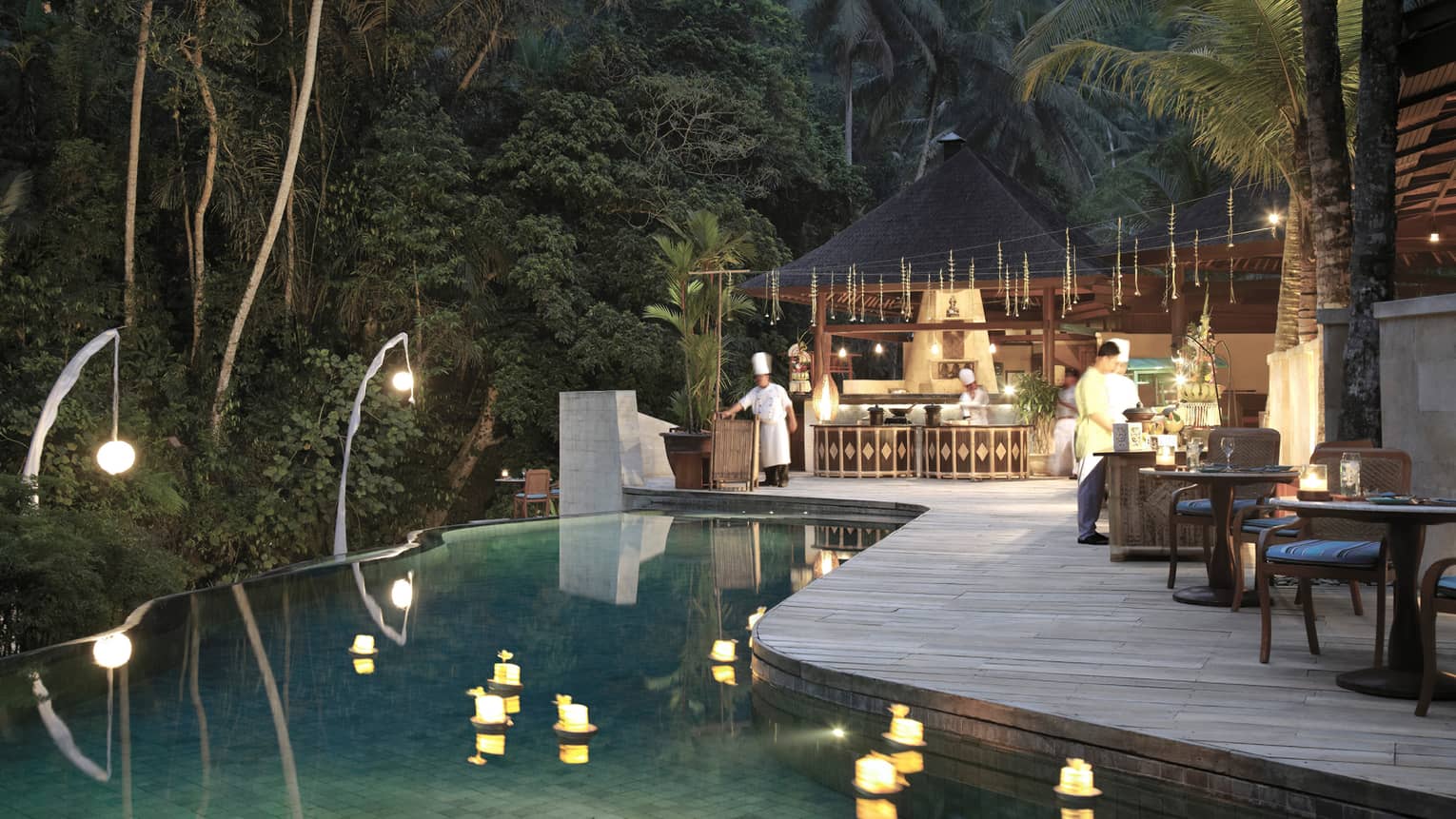 An infinity pool looking out towards the dense jungle; chefs bustle around the outdoor kitchen on the poolside deck.