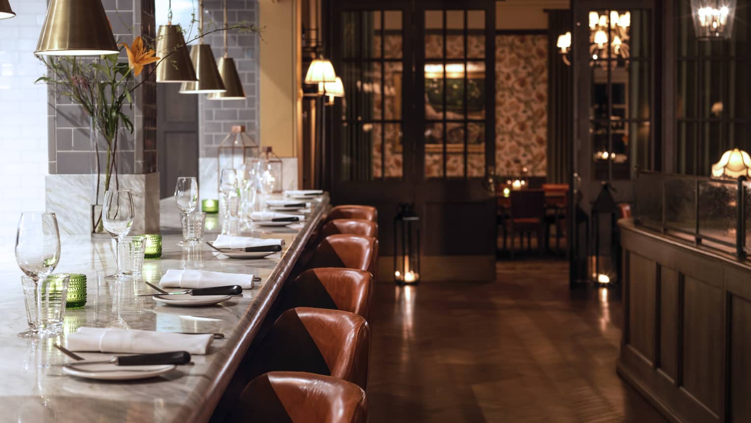 Long white marble dining bar with plates, cloth napkins, wine glasses, brown leather stools