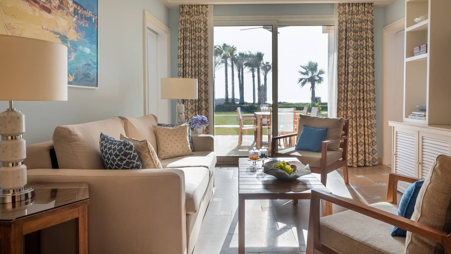 Guest room living area with tan sofa and armchairs, coffee table, sliding glass door to patio