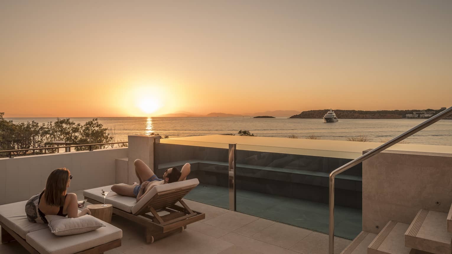 Couple relaxes on plush lounge chairs on Nafsika One Bedroom Terrace Suite with Pool deck