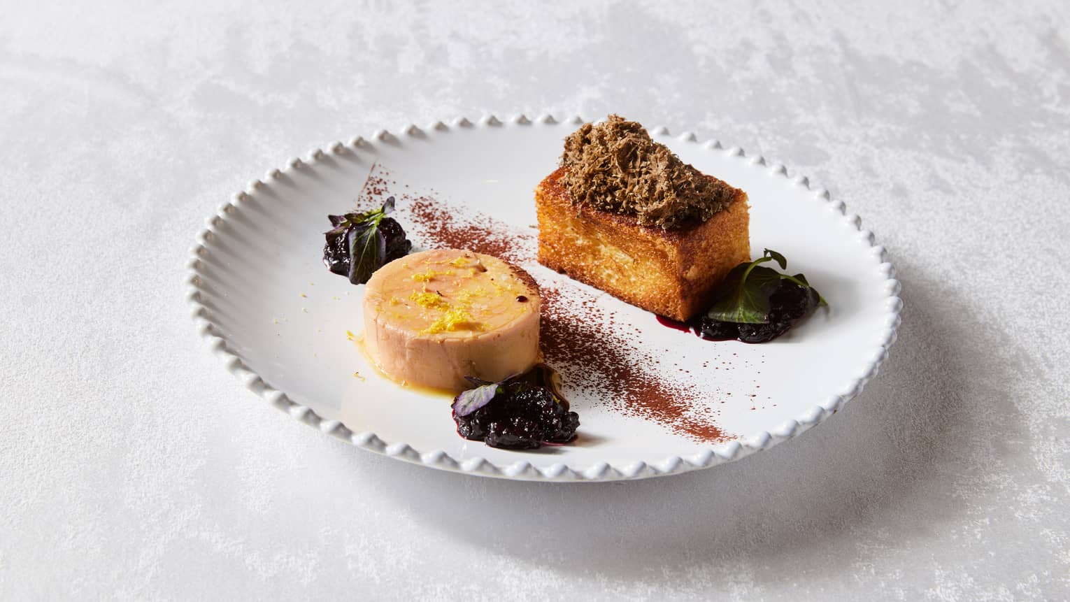 One square-shaped dessert and another round-shaped dessert on a plate with toppings.