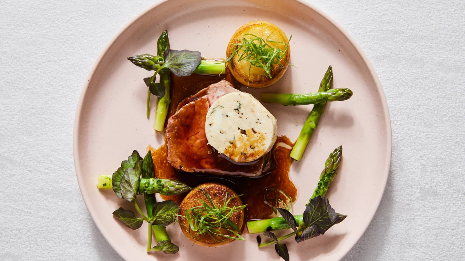 Asparagus arranged on a plate around the main dish with green toppings.