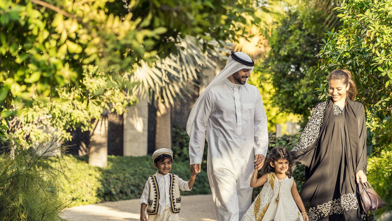 Two adults and two young children walk smiling through a pathway lined with lush trees and greenery
