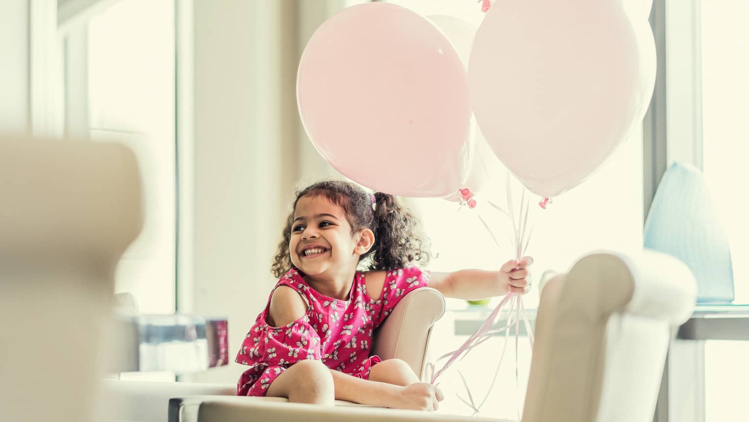 Child smiling whilst holding pink balloons