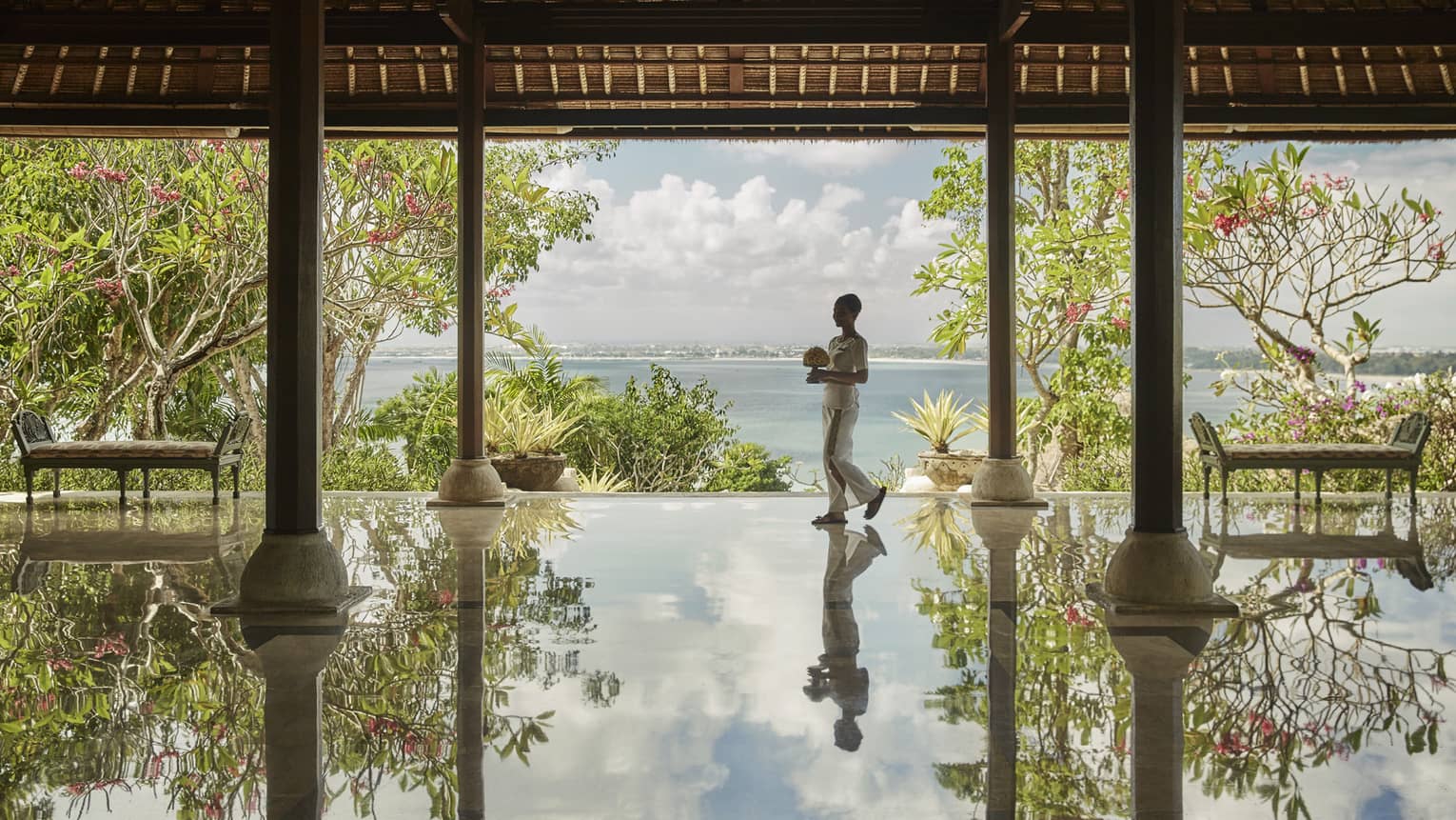 Hotel staff carrying flowers reflected onto floor of open-air pavilion 