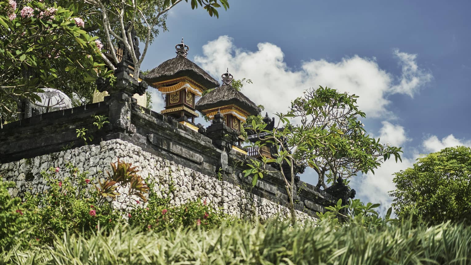 Exterior view of resort temple with stone wall, posts and carvings, tropical trees