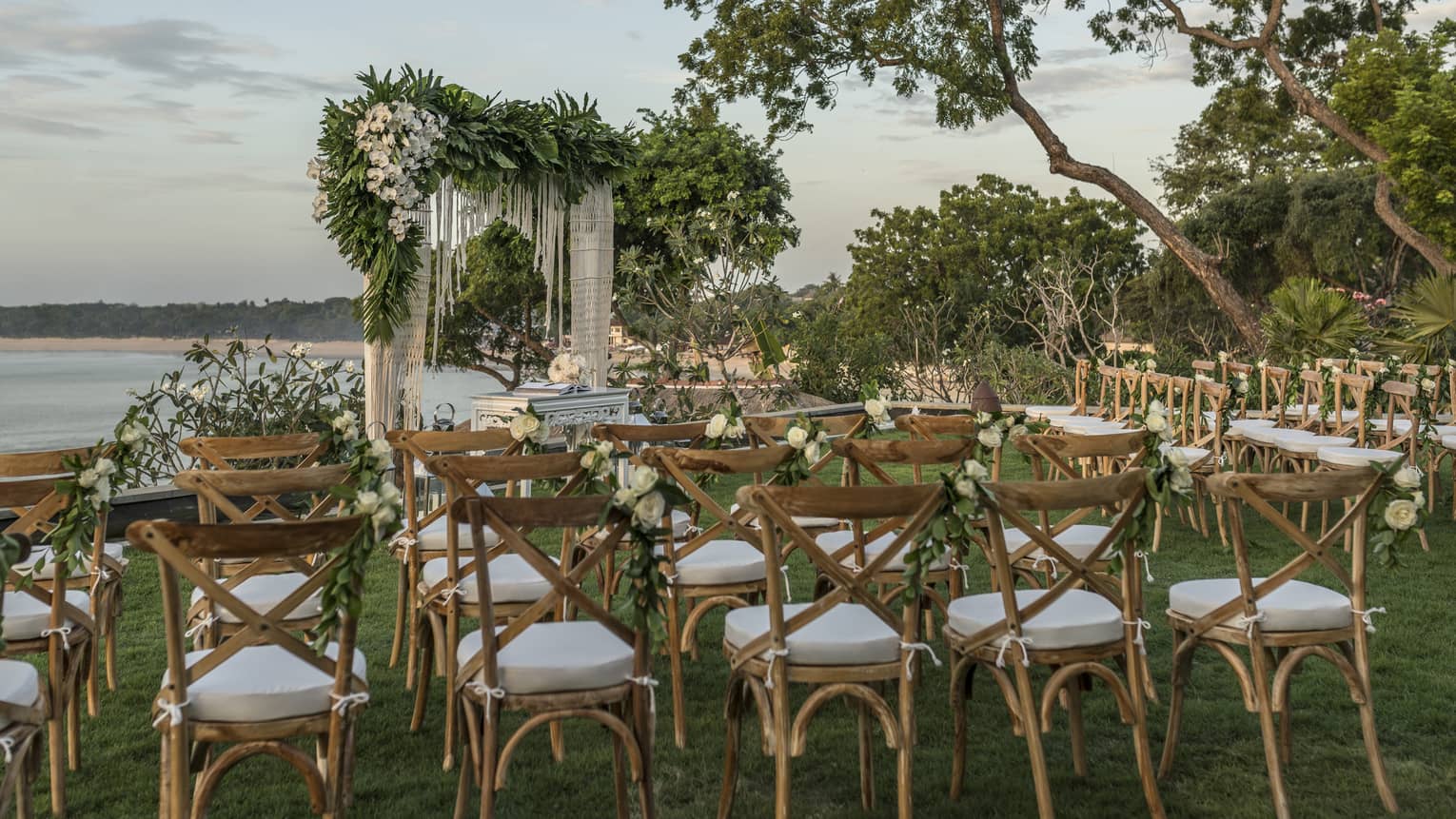 Rows of chairs face wedding altar with flowers on lawn overlooking ocean