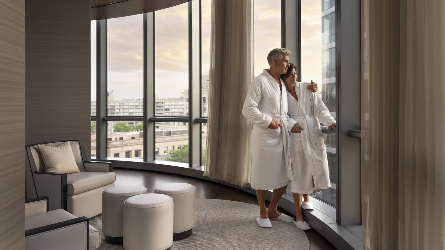 A man and woman in spa robes looking out a window.
