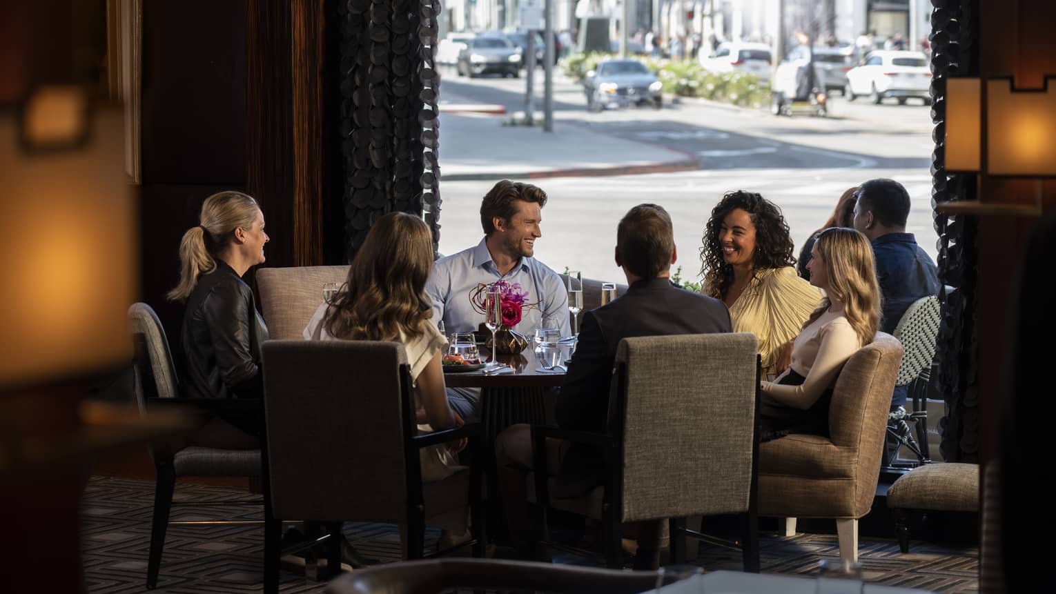 A group of people sitting around a large round table with a view of a road outside.