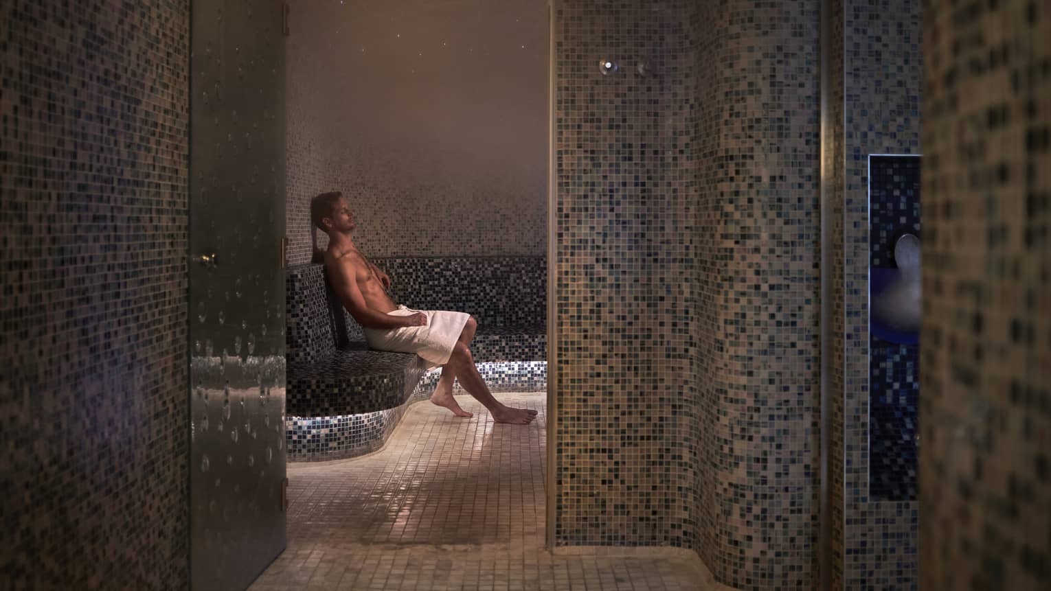 A man sitting with a towel in a dimly lit spa room.