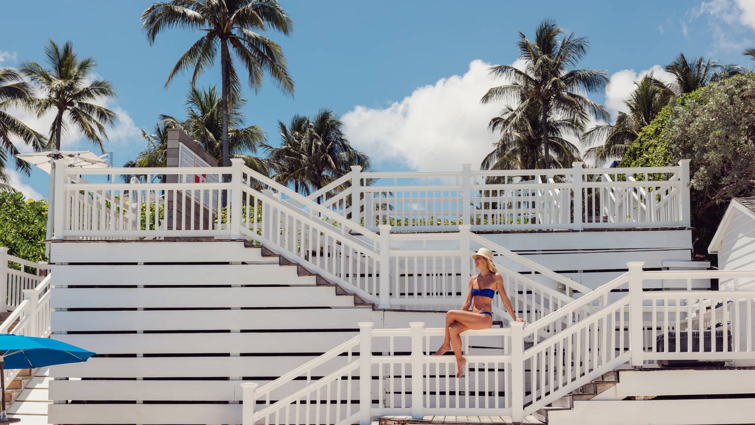 A person wearing a swimsuit and sitting on a staircase leading to the shore