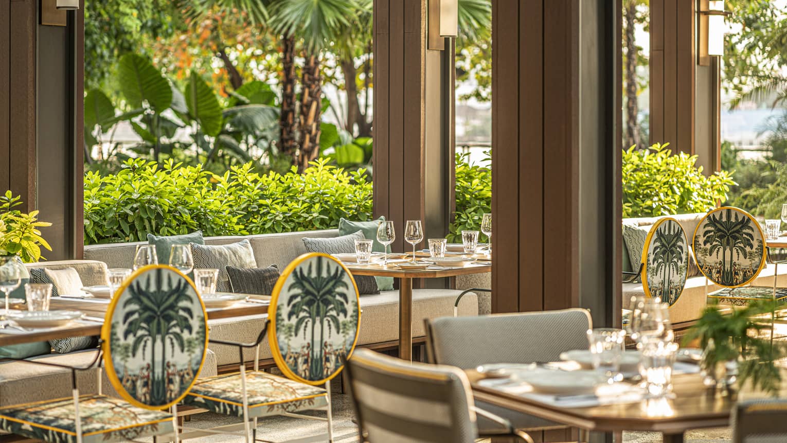 Elegant outdoor dining area with neatly set tables, palm-themed chairs and lush greenery surrounding the seating area, creating a tropical ambiance