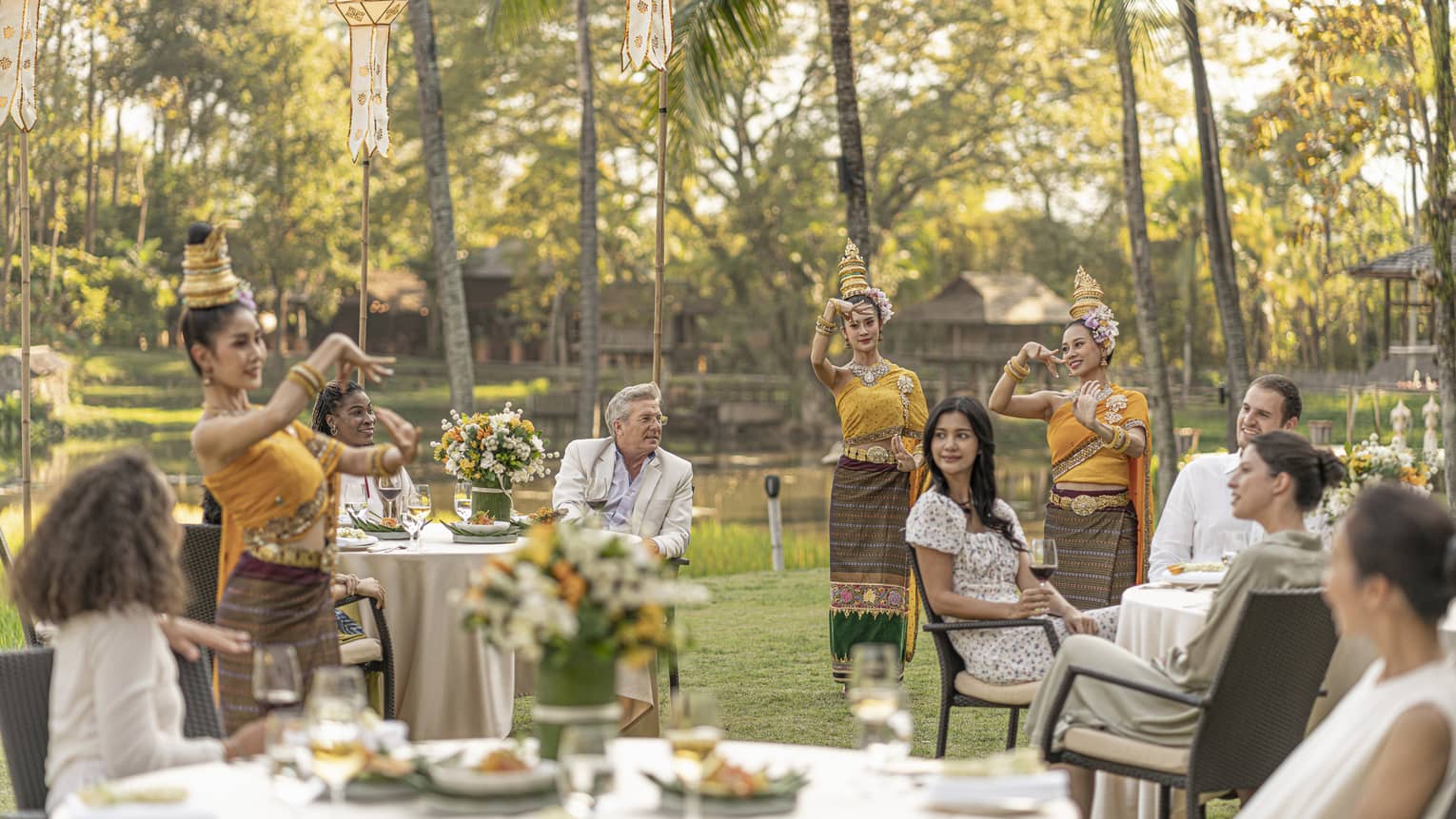 People in white sitting at various tables, as Thai dancers in yellow gowns perform in front of them.