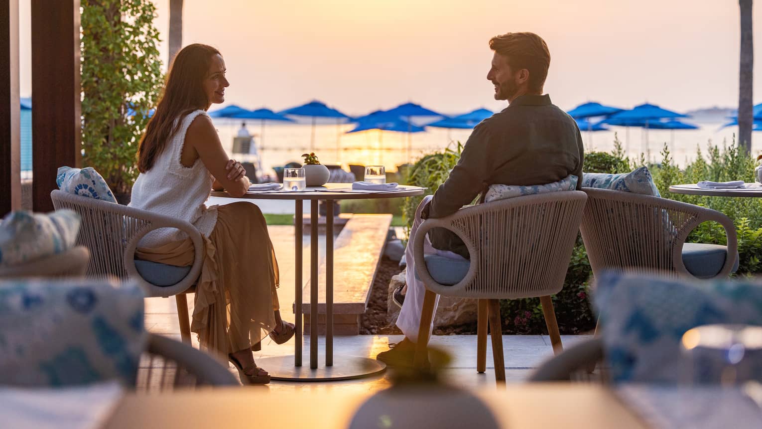 Couple sits at a table overlooking the ocean at sunset